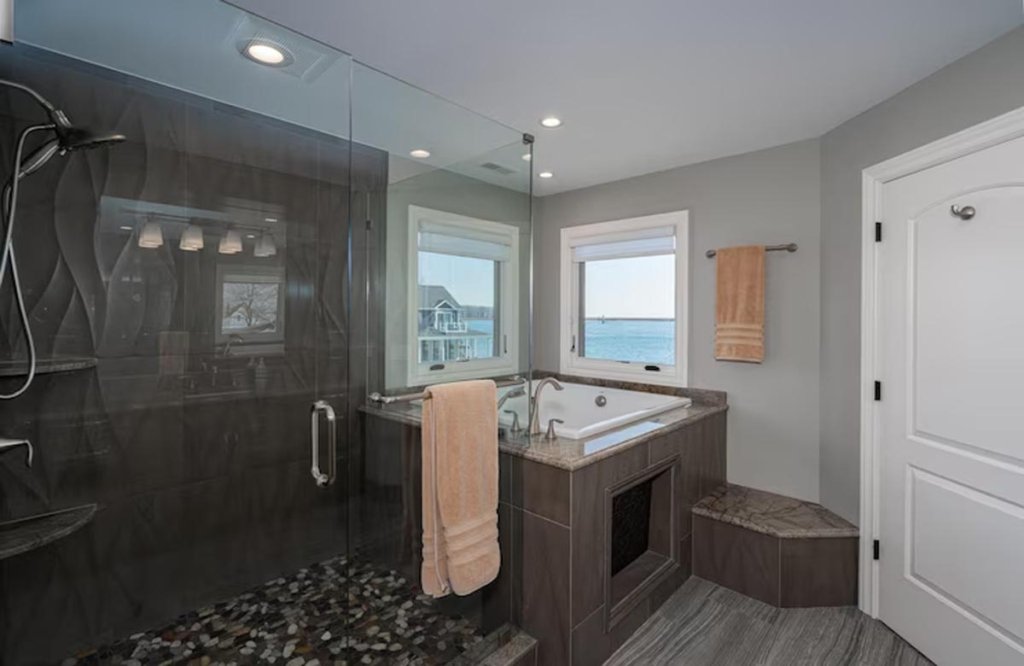 Bathroom renovation contractors transformed this space with spa-like finishes, stunning tilework, and a soaking tub overlooking serene waterfront views.