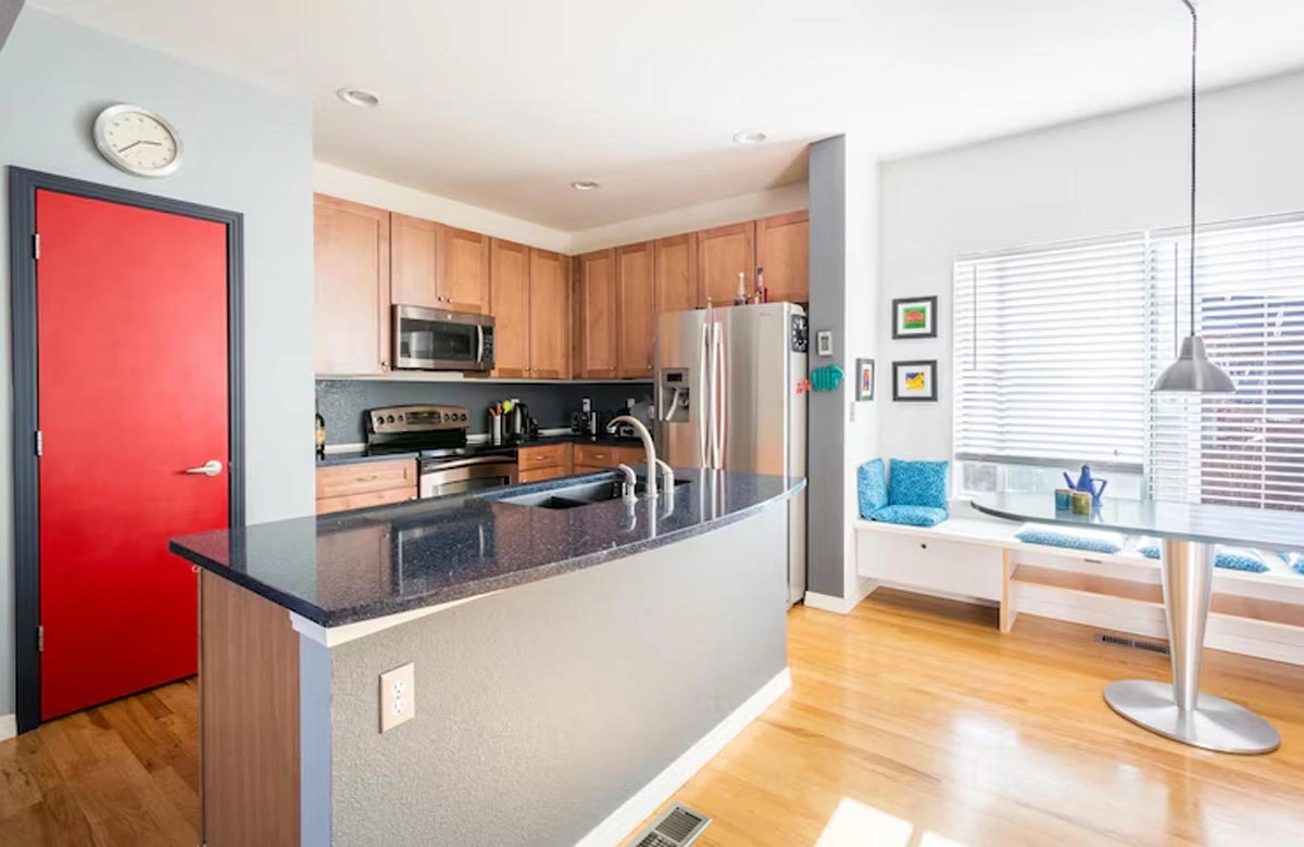 This vibrant kitchen renovation in Austin showcases a bold red door, cozy breakfast nook, and contemporary finishes for a cheerful, efficient layout.